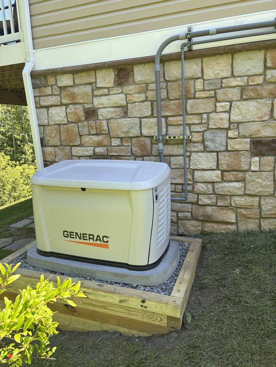 New Generac standby generator on a gravel pad beside a stone-faced home, installed by RJ